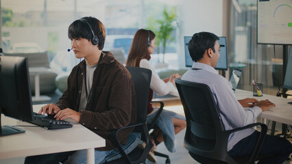 Focused Asian man provides tech support in customer service call center. An operator works...
