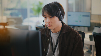 Confident Asian businessman provides tech support in a diverse call center office. He wears a...