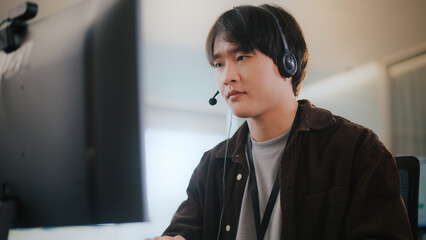 Confident Asian businessman provides tech support in a diverse call center office. He wears a...