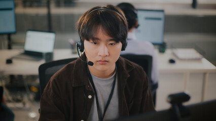 Serious young asian man working in call center providing tech support customer service. operator...