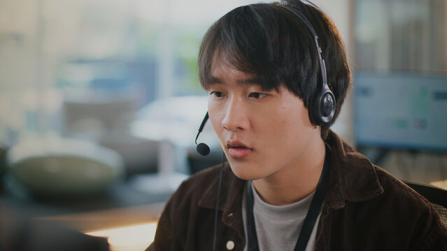 Surprised asian man working at tech support call center providing customer service. Young operator looks confused while on headset call assisting client with problem