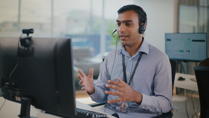 Focused Indian man at tech support call center provides professional customer service. He uses...