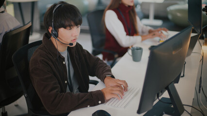 Focused young Asian man provides tech support and customer service at call center. Operator with...