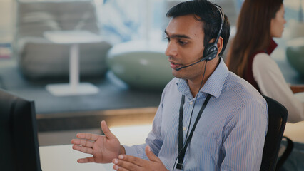Focused Indian male tech support agent provides helpful customer service from modern call center....