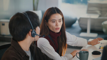 Focused woman provides tech support training for customer service agent in modern call center. She...