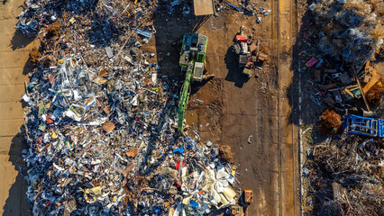 Aerial view of a scrapyard with a material handler sorting metal waste. Piles of scrap and industrial surroundings.