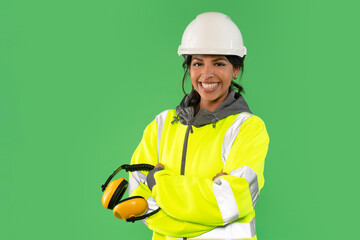 Confident worker in reflective safety gear poses with headphones against a green background,...