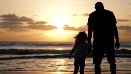 Father and daughter hold hands walking on beach at golden sunset, happy family moment - Powered by Adobe