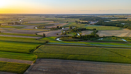 Aerial view of the meandering Prosna River surrounded by agricultural fields during sunset. Picturesque rural landscape with warm evening light and winding river