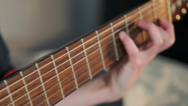 Female hand gently plucking nylon strings of a classical guitar at home. Detailed close-up showing finger movement. Concepts like hobby and creativity.