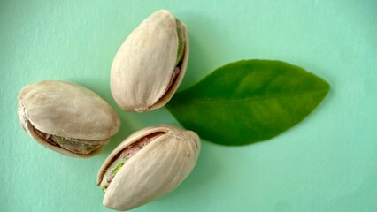 Minimalistic close-up of three open pistachio nuts with a fresh green leaf on a mint green background. Organic vegan snack concept with natural colors and textures.