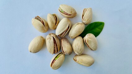 A pile of pistachios in shells and a green leaf on a white background