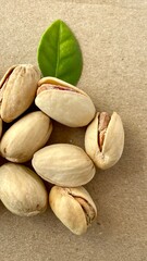 A pile of pistachios in shells and a green leaf on a gray paper background