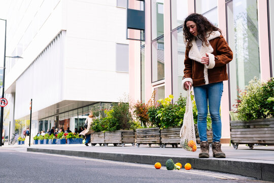Woman outdoors in urban London dropping fruit from bag on city street