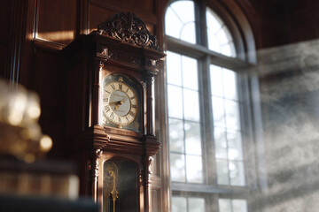 Antique grandfather clock standing tall against a sunlit window. Evokes feelings of history, timelessness, and tradition. Perfect for portraying legacy or mortality.