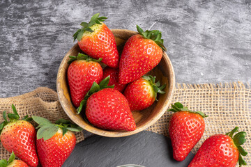 Fresh strawberries with green leaves arranged on a gray stone surface.