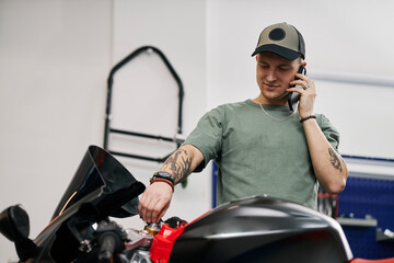 Mechanic repairing motorcycle while talking on smartphone in workshop