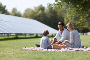 Family enjoying a picnic on a lawn with solar panels in the background. Represents sustainable living, renewable energy, and a modern, ecoconscious lifestyle.