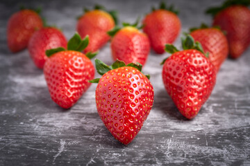 Fresh strawberries with green leaves arranged on a gray stone surface.