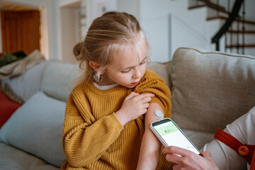 Mother checking child's glucose sensor at home on the sofa
