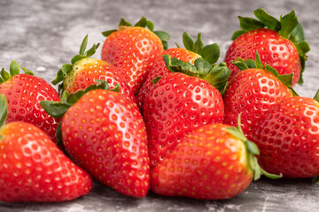 Fresh strawberries with green leaves arranged on a gray stone surface.