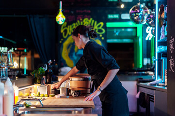 Chef in uniform preparing sushi at modern restaurant kitchen at night
