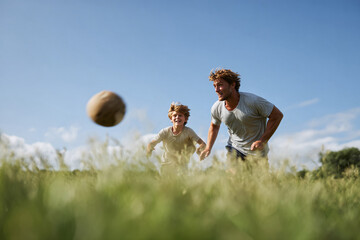 A father and son play soccer together in a sundrenched meadow under a blue sky. Represents family, bonding, recreation, sport, and the joy of simple moments. Ideal for lifestyle  familythemed content.
