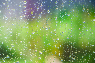 Water droplets on a glass surface, with a blurred background of lush greenery, symbolizing a...