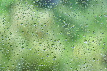 Water droplets on a glass surface, with a blurred background of lush greenery, symbolizing a...