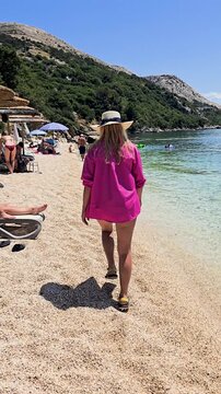 Young Woman Walking Along the Beach at Stara Baska Skrila Camp on a Sunny Summer Day. Peaceful Coastal Scenery, Clear Sea, and Relaxed Atmosphere in a Natural Seaside Setting FKK Beach