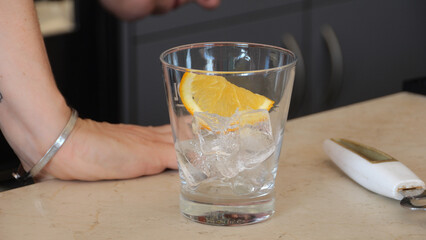 Mixologist garnishing orange infused cocktail with citrus slice, dropping vibrant wedge into frosty...