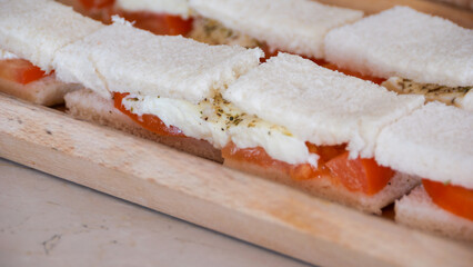Wooden cutting board displaying layered sandwiches. Mozzarella slices, ripe tomatoes, sprinkled...