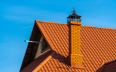 A striking brick chimney rises from a vibrant red tiled roof, contrasting beautifully with the...