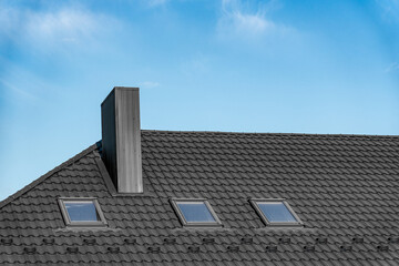 A contemporary structure showcases a stylish roof featuring skylights, blend of materials, and sleek chimney under a bright blue sky