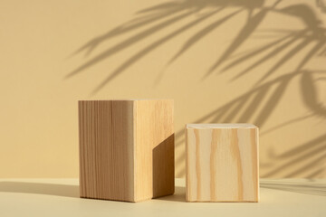 Wooden cube-shaped scenes with the shadow of tropical palm leaves on a beige background. A premium geometric podium for advertising your product. Showcase, display case.