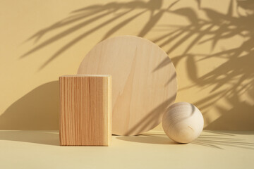 Wooden scenes of different geometric shapes with a shadow of tropical palm leaves on a beige...