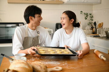 An Asian Couple holds a tray of shaped cookie dough, ready to go in the oven, surrounded by freshly baked bread and laughter