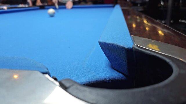 Red billiard ball falling into corner pocket on blue pool table with cue ball in background. Sports game and recreation video footage. Close up view