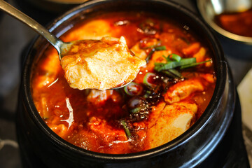 Eating Sundubu-jjigae, the beloved Korean soft tofu stew, served in a traditional black earthenware pot. This authentic Korean dish is a popular choice for a hearty, spicy, and warming meal.