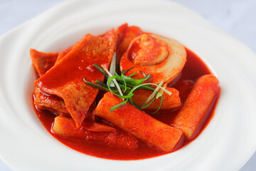 Close-up view of Tteokbokki, a Korean street food. This dish features rice cakes (tteok), savory fish cakes (eomuk), fresh green onions, and a halved boiled egg, all coated in a red gochujang sauce.