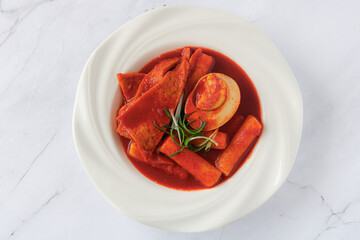 Top view of Tteokbokki, a Korean street food. This dish features rice cakes (tteok), savory fish cakes (eomuk), fresh green onions, and a halved boiled egg, all coated in a red gochujang sauce.
