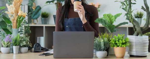 Remote Work. Young woman enjoying coffee in a plant-filled workspace, focused on her laptop.