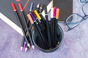 A black cup filled with colored pencils next to reading glasses