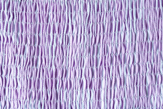 Close-up texture of smocked fabric, showcasing its parallel rows and delicate stitching in shades of purple. This textile background gives depth and elasticity, ideal for fashion and craft projects.