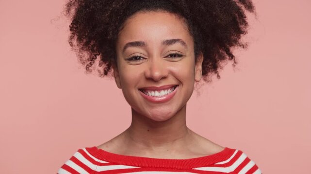 Smiling woman winking playfully at camera on pink background
