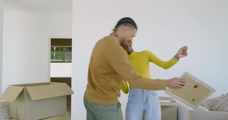 Diverse couple unpacking moving boxes, examining picture frame, dancing at home celebrating move in - Powered by Adobe