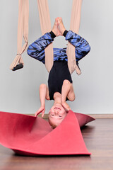 Young male child with light hair hangs inverted in aerial hammock indoors. Smiling while suspended...