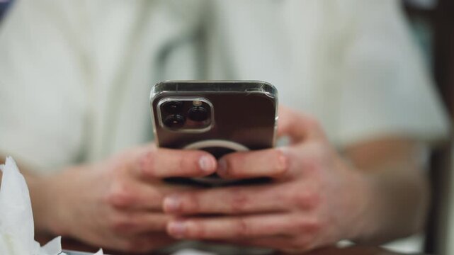 White man hand showing some reddish knuckles holding black apple phone in clear pouch while pressing screen closeup, soft background blur, focus on beauty, gesture and protective case