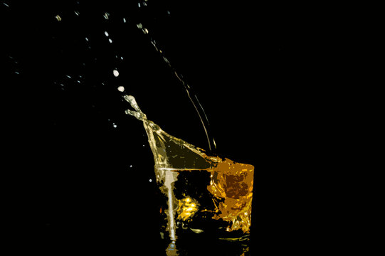 vaso de wiski con tonalidades amarillas y fondo oscuro salpicando cuando cae el hielo