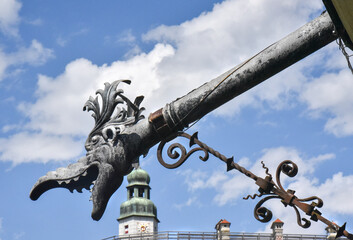 An ornate downspout shaped like a basilisk head decorates the end of a historic gutter in...
